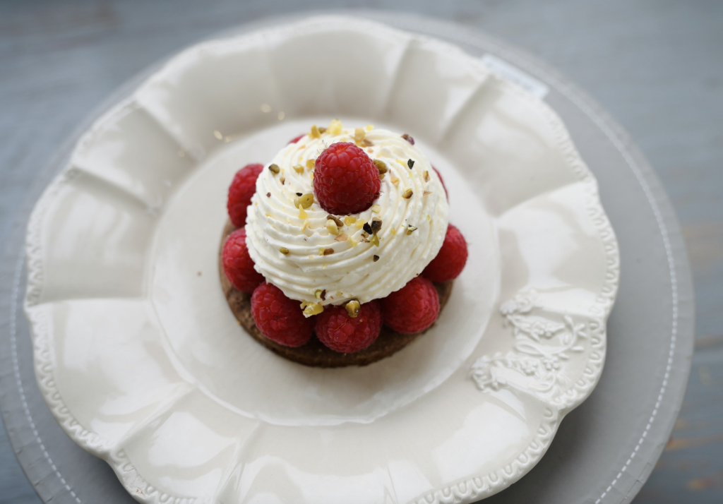 Tartelette aux framboises avec chantilly maison et éclats de pistache sur une assiette blanche